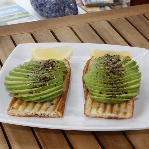 Two avocado toasts with chili flakes and lemon wedges on a white plate at Le Fernández Café.