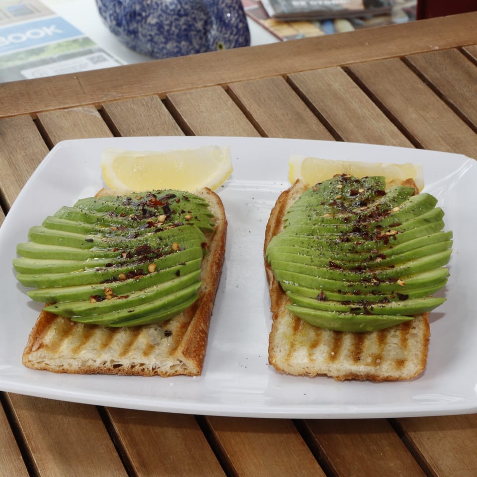 Two avocado toasts with chili flakes and lemon wedges on a white plate at Le Fernández Café.