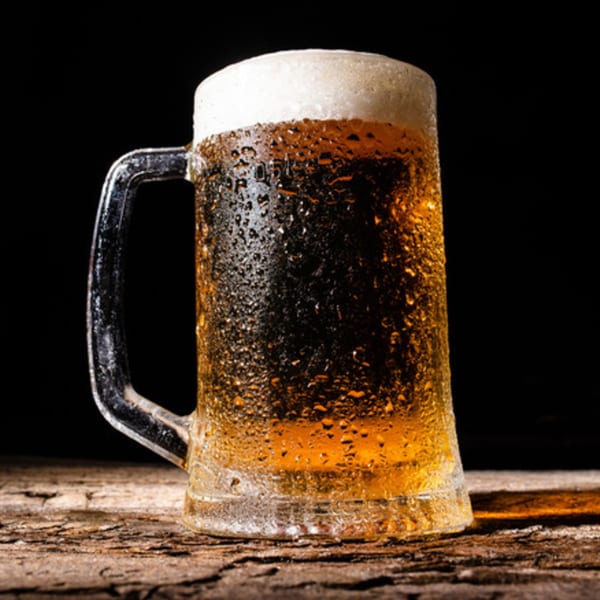 A frosty mug of beer with a foamy head and condensation sits on a rustic wooden table.