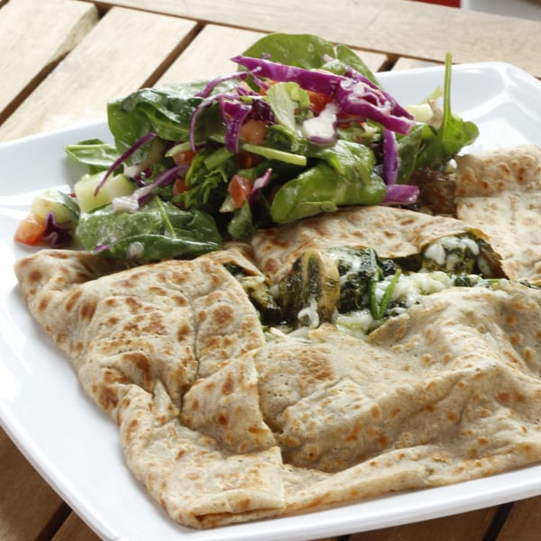 Savory crêpes filled with spinach and cheese, served with a fresh green salad on a white plate.
