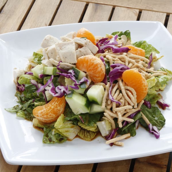 A vibrant chicken salad with mandarin oranges, cucumbers, and crispy noodles on a white plate.