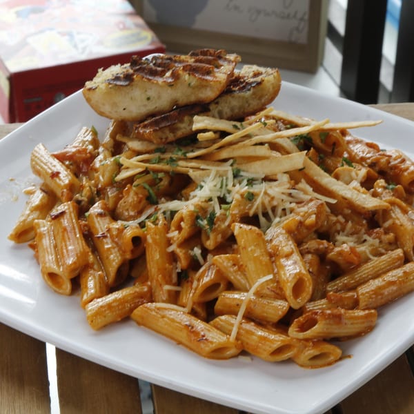 Penne pasta with creamy sauce, shredded cheese, tortilla strips, and grilled bread on a white plate.