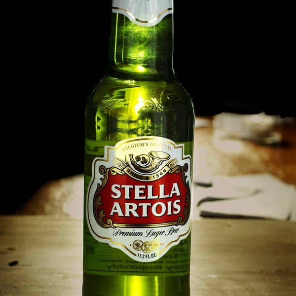 Close-up of a green Stella Artois beer bottle with a red and gold label on a wooden surface.