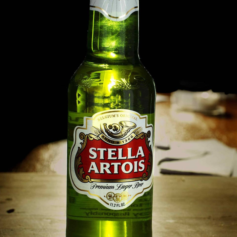 Close-up of a green Stella Artois beer bottle with a red and gold label on a wooden surface.