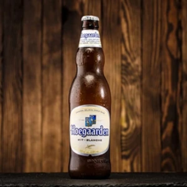 A cold, condensation-covered bottle of Hoegaarden beer stands against a rustic wooden background.