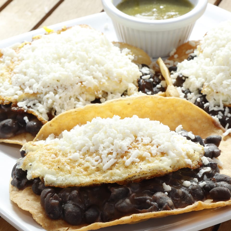 Le Fernández Café's huevos rancheros with black beans, fried eggs, and crumbled cheese, with green salsa.