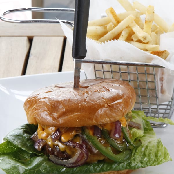 A burger with melted cheese, grilled onions, and green peppers, served with fries in a metal basket.