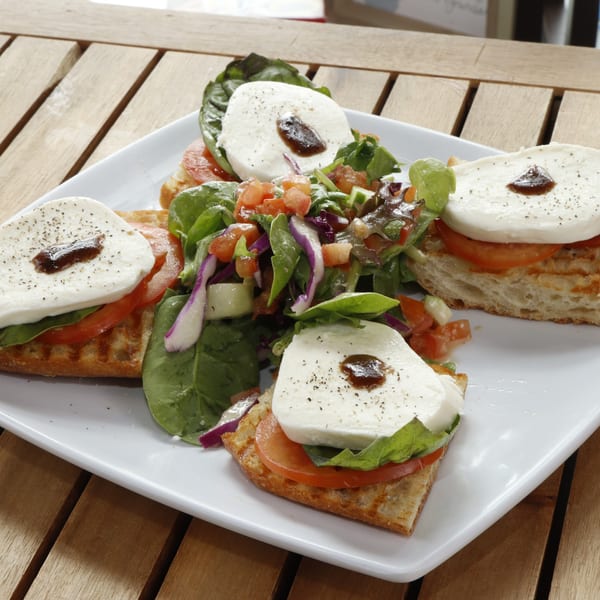 Four bruschetta with mozzarella, tomato, basil, and balsamic glaze, served with a side salad.
