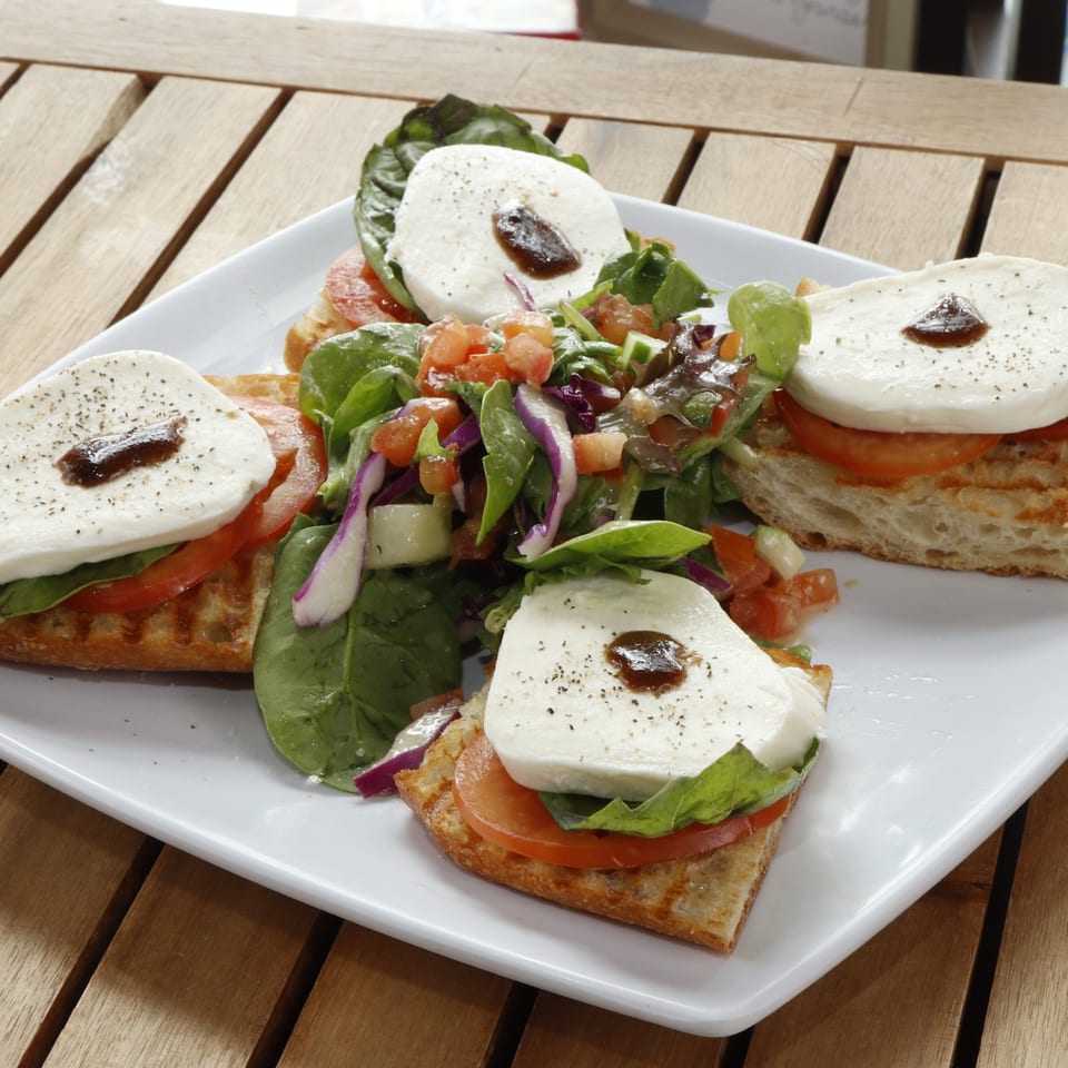 Four bruschetta with mozzarella, tomato, basil, and balsamic glaze, served with a side salad.
