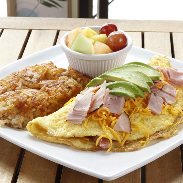A Le Fernández Café omelet with ham, cheese, avocado, hash browns, and a fruit cup.